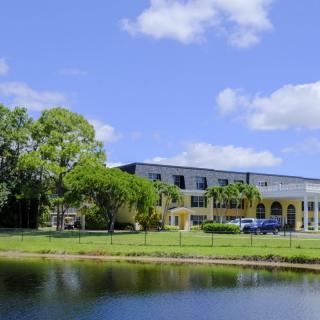 A building by a lake surrounded by trees under a bright blue sky.