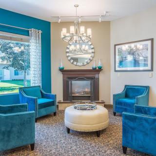 A cozy living room with blue chairs and a fireplace, featuring elegant decor including a mirror and chandelier.