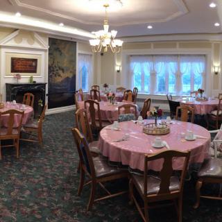 An elegant dining room with round tables, set for a formal event, featuring chandeliers and decorative elements.