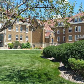 A sunny day with a view of a large, brown brick building surrounded by green grass and trees.