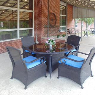 A patio setting with wicker chairs and a glass-top table against a brick wall.