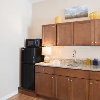 A compact kitchen area with wooden cabinets, a refrigerator, microwave, and decorative elements.