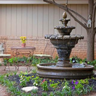 A serene garden patio featuring a decorative fountain surrounded by colorful flowers and outdoor seating.