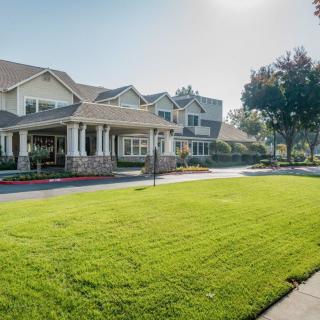 A large suburban house with a green lawn and trees under bright sunlight.