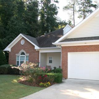 A suburban house with a brick exterior, attached garage, and well-maintained lawn surrounded by trees.