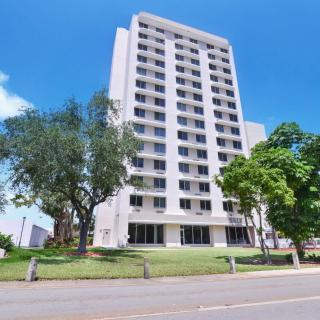 A tall, white high-rise building surrounded by trees under a clear blue sky.