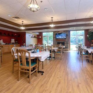 A cozy dining area with wooden floors, tables, and chairs, lit by chandeliers and a large window view.