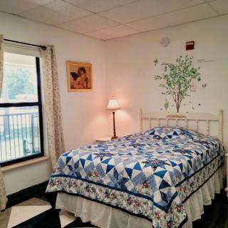 A cozy bedroom with a quilt-covered bed, a lamp, and wall decorations.