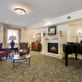 A cozy living room with a fireplace and grand piano, featuring elegant furniture and warm lighting.