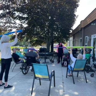 A group of seniors participates in an outdoor exercise session on a sunny day.