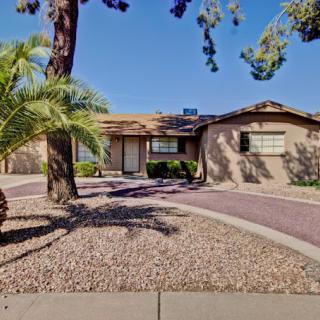 A single-story house with a landscaped yard and palm trees in a desert climate.