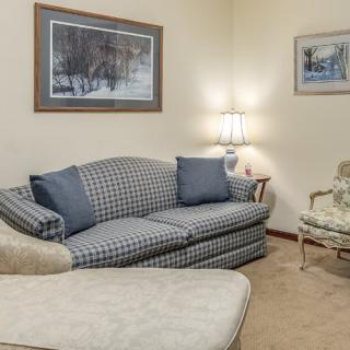 A cozy living room with a plaid sofa, cushioned armchair, and warm lighting from a table lamp.