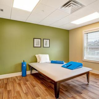 A serene therapy room featuring a minimalist design with a comfortable bed, bright natural light, and soothing green walls.