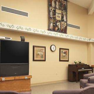 A living room featuring a television, a piano, framed artworks, and a wall clock.