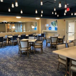 A modern dining area featuring neatly arranged tables and chairs, illuminated by stylish ceiling lights.