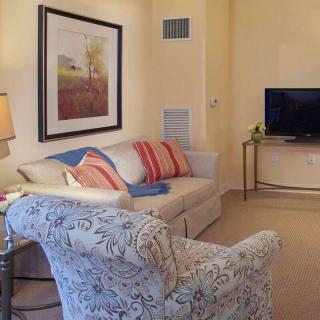 A cozy living room with a sofa, armchair, and television, featuring artwork on the wall.