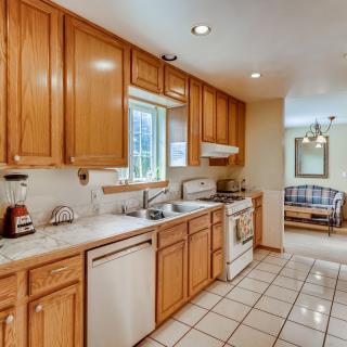 A spacious kitchen with wooden cabinets and a tiled floor, featuring modern appliances and bright natural lighting.