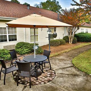 A cozy outdoor patio with a table, chairs, and an umbrella situated in a well-maintained garden area beside a house.