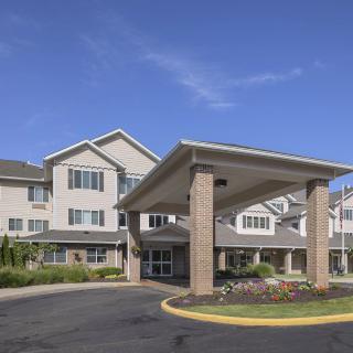 A modern residential building with a covered entrance and well-maintained landscaping under a clear blue sky.