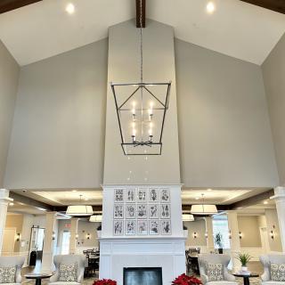A modern living room with a high ceiling, featuring a central chandelier and a fireplace.
