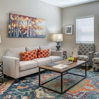 A cozy and stylish living room with a comfortable sofa, colorful pillows, a wood and metal coffee table, abstract artwork, and modern lighting.