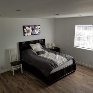 A minimalist bedroom with a simple bed, artwork on the wall, and natural light from a window.