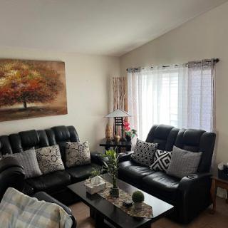 A cozy living room featuring black leather sofas, decorative cushions, and a vibrant piece of artwork.