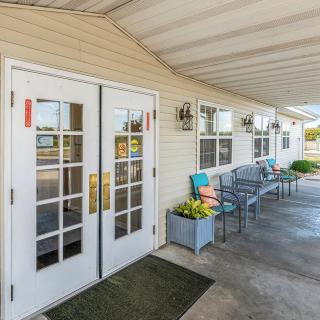 A welcoming building entrance with large glass doors, benches, and flower decorations under an awning.