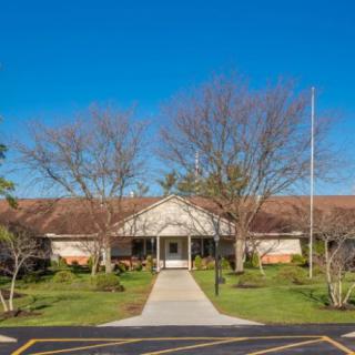 The front view of a library with a pathway leading to the entrance, surrounded by trees under a clear blue sky.