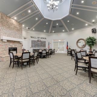 A spacious dining area with multiple tables and chairs, featuring a chandelier, fireplace, and a 'Wall of Honor' display.