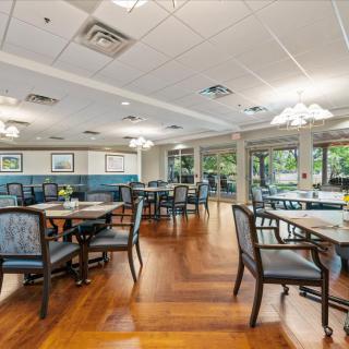 A spacious dining area with neatly arranged tables and chairs, featuring wooden flooring and ceiling lights.