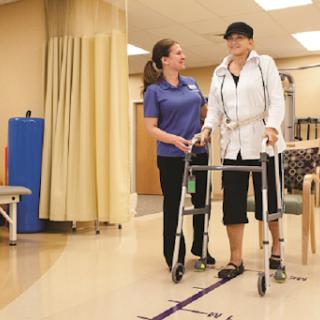 A patient uses a walker during physical therapy with the assistance of a therapist.