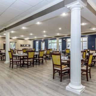 A spacious dining room with multiple tables and chairs, featuring elegant columns and bright lighting.