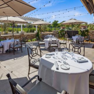 An elegant outdoor dining area with tables set under large umbrellas and decorative string lights, perfect for a sunny day.