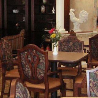 A cozy dining area featuring ornate chairs, a wooden table with a vase of flowers, and decorative elements in the background.
