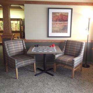 A cozy seating area with a checkers board on the table, flanked by two chairs and lit by a floor lamp.