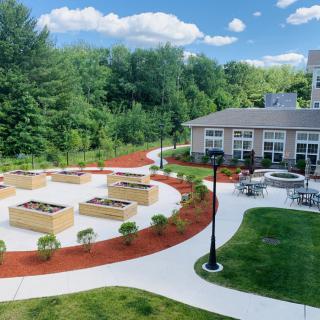 A beautifully landscaped outdoor area featuring raised garden beds, a building, and winding walkways surrounded by lush greenery.