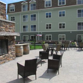 Outdoor patio area with chairs and a fireplace in front of a residential building.
