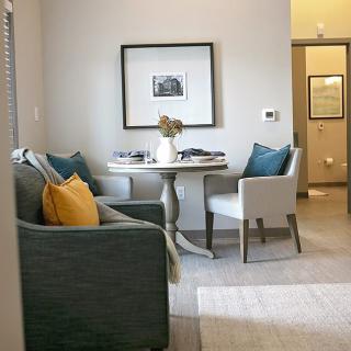 A cozy living and dining space featuring a round table with chairs and a comfortable armchair, accented by colorful cushions and wall art.