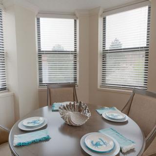 A cozy dining area with a round table set for four, bathed in natural light from large windows.
