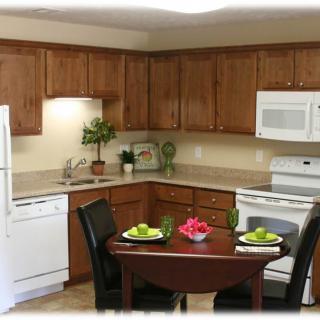 A cozy kitchen with wooden cabinets featuring a small dining table set for two, and equipped with modern appliances.
