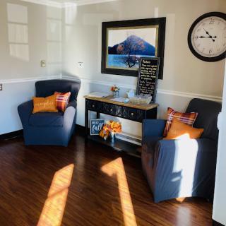 A cozy living room setup featuring two blue chairs with decorative pillows, complemented by a stylish clock and artwork on the wall.