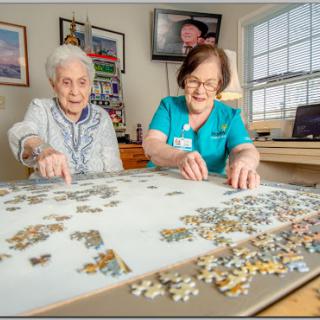 A caregiver and an elderly woman enjoy a fun puzzle activity together, fostering social interaction in a bright and welcoming indoor space.