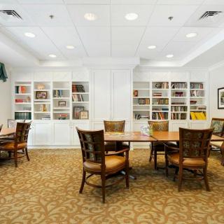 A well-lit library room with bookshelves, tables, and chairs for reading.