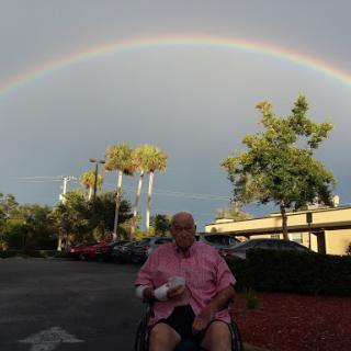 A serene moment captured under a vibrant rainbow, with an individual in a wheelchair enjoying the outdoors.