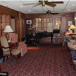 A cozy living room with wood paneling, featuring a piano, various seating options, and warm lighting.