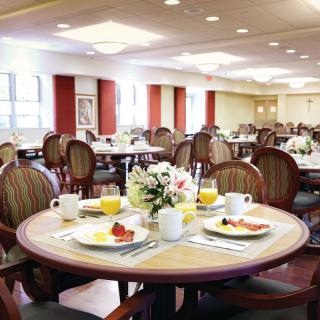 A spacious dining room set up for breakfast with neatly arranged tables, complete with tableware and floral centerpieces.