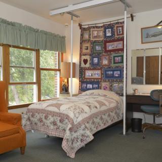 A cozy bedroom with a quilt-covered bed, an orange armchair, and large windows.