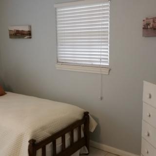 A cozy bedroom with a wooden bed, dresser, and window with blinds.