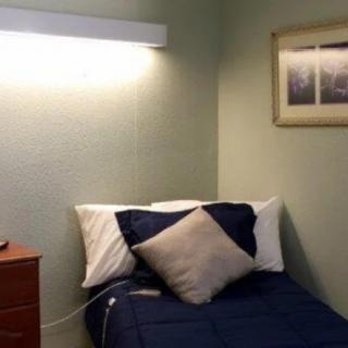A small bedroom featuring a single bed with blue bedding, a nightstand, and a wall-mounted lamp.